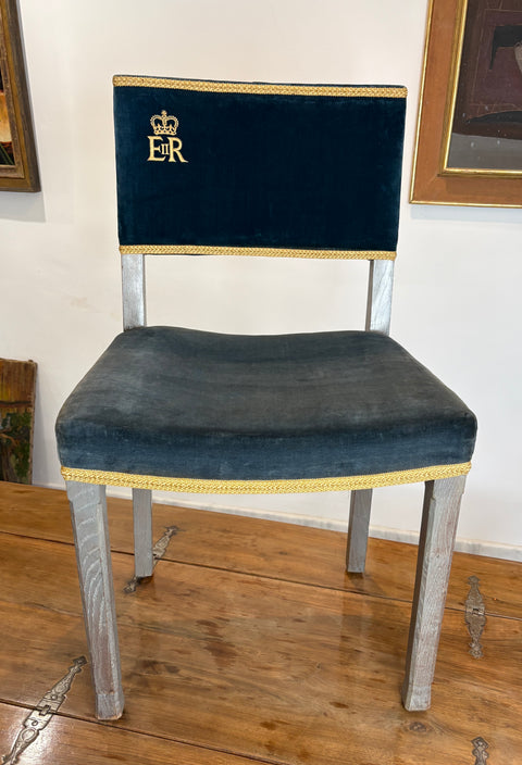 Chair with navy velvet seat and backrest, gold trim, and 'ER' emblem on a wooden floor.