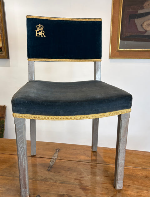 Navy velvet chair with gold trim and emblem on a wooden floor.