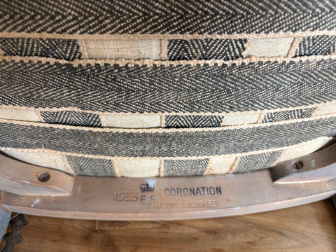 Close-up of a woven chair seat with 'Coronation' branding on a wooden floor.